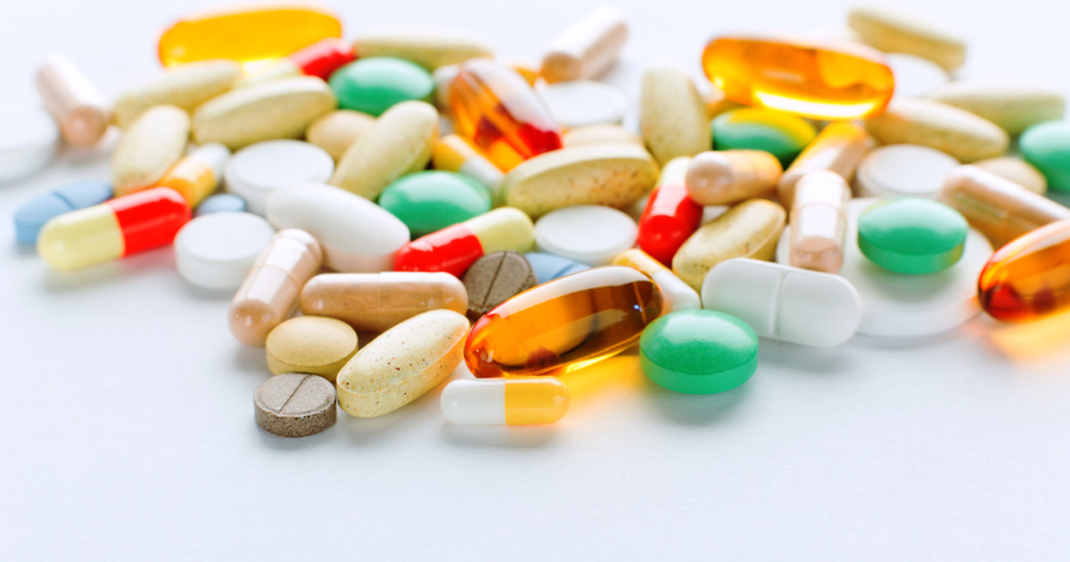 A variety of colorful pills and capsules are scattered on a white surface. The assortment includes round tablets, oval capsules, and gel capsules in various colors such as yellow, green, orange, and white. When considering "What Should I Look for In a Supplement," evaluate the ingredients carefully.