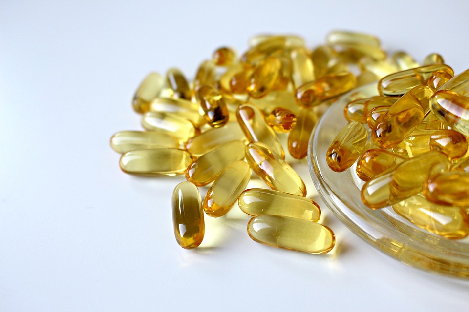An assortment of yellow, translucent gel capsules, known as some of the best supplements, is spread on a white surface. Some capsules are gathered in a clear, shallow dish on the right side of the image.