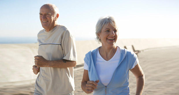 An older man and woman, both advocates for Omega-3, are jogging together outdoors on a sunny day. They are smiling and appear to be enjoying their exercise, promoting a lifestyle to combat Alzheimer’s. The background shows a clear blue sky and a paved path; she wears a light blue jacket while he sports a light grey shirt.