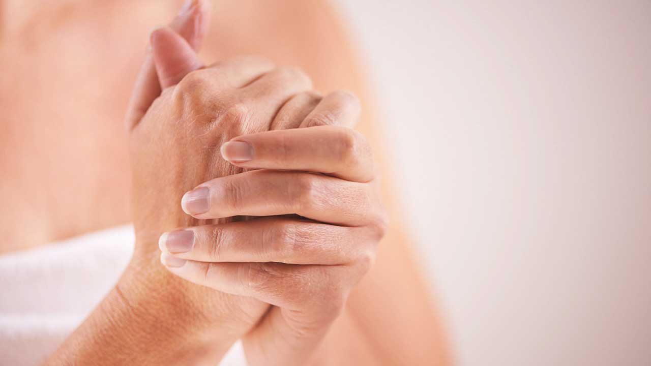 Close-up image of a person's hands clasped together. The hands are the focal point, with soft lighting highlighting the skin's texture, resembling one of the 7 Psoriatic Arthritis Signs You Thought Were Something Else. The background is blurred and neutral in color, emphasizing the hands' delicate and caring gesture.