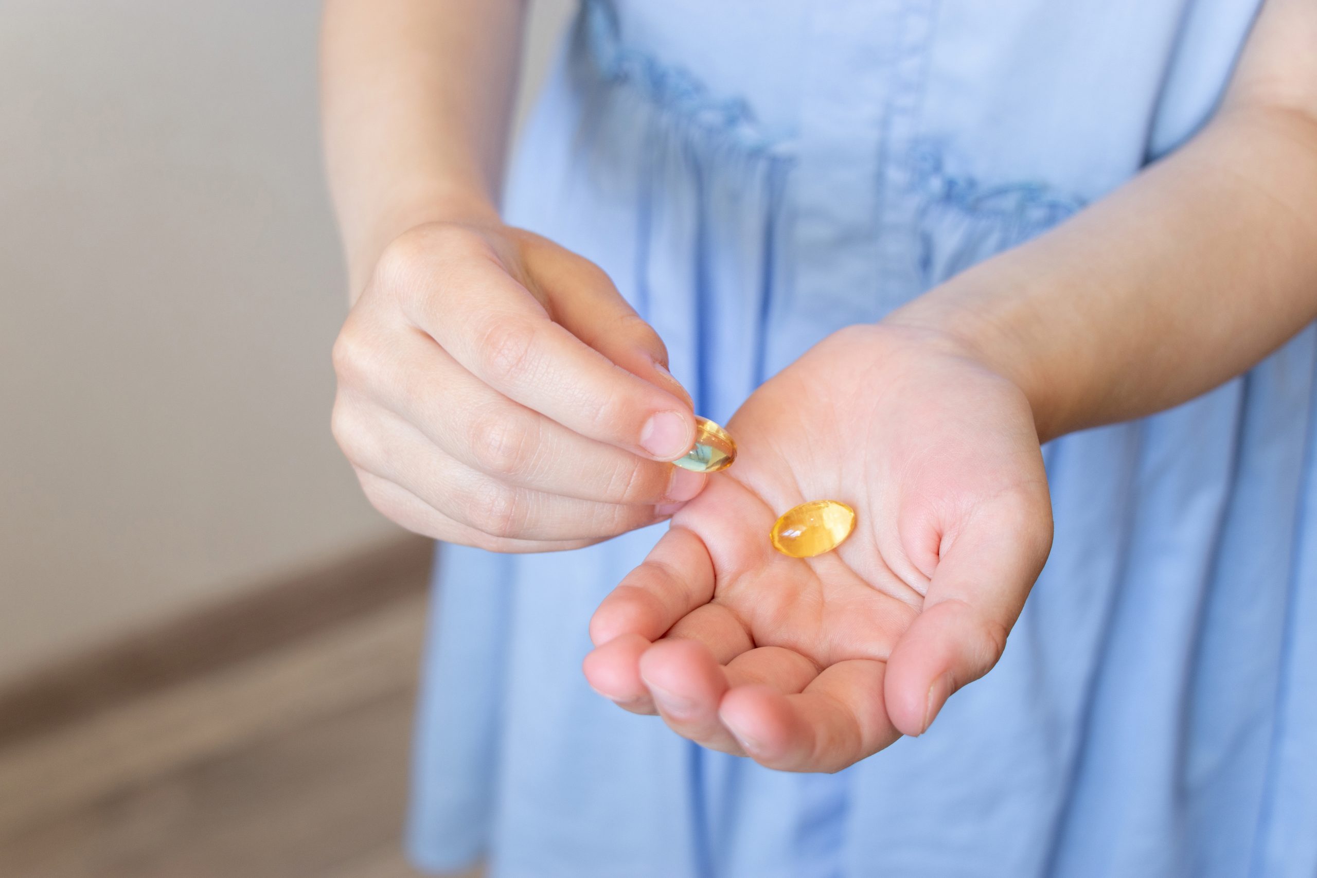 A person in a light blue dress holding a clear goldfish cracker in one hand and another smaller goldfish cracker in the other hand. The background is blurred, focusing attention on the hands and crackers.