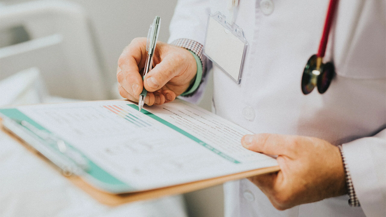 A medical professional wearing a white coat, identified by a stethoscope around their neck and an ID badge, is holding a clipboard. As they focus on filling out patient information, their mind briefly ponders the question: Do antibodies cause inflammation?