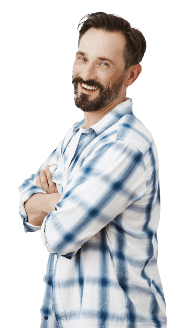 A smiling man with a beard and mustache stands with his arms crossed. He is wearing a blue and white plaid shirt and has dark hair with a bit of gray. The background is white.