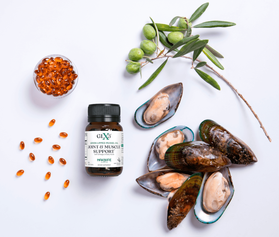 A bottle of GLX3 Joint & Muscle Support supplement is surrounded by green-lipped mussels, a branch with green olives, and scattered soft gel capsules, with a small transparent bowl filled with the same capsules nearby—ideal for those mindful of shellfish allergies.