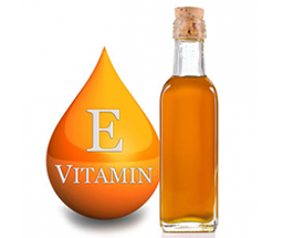 A small glass bottle filled with a golden liquid stands next to an orange droplet-shaped icon. The icon features the letter "E" and the word "VITAMIN" below it, indicating Vitamin E.